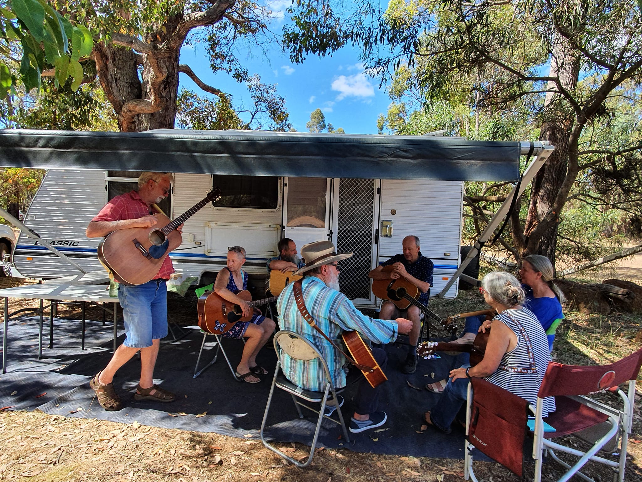 people sitting in front of a caravan participating in a guitar workshop